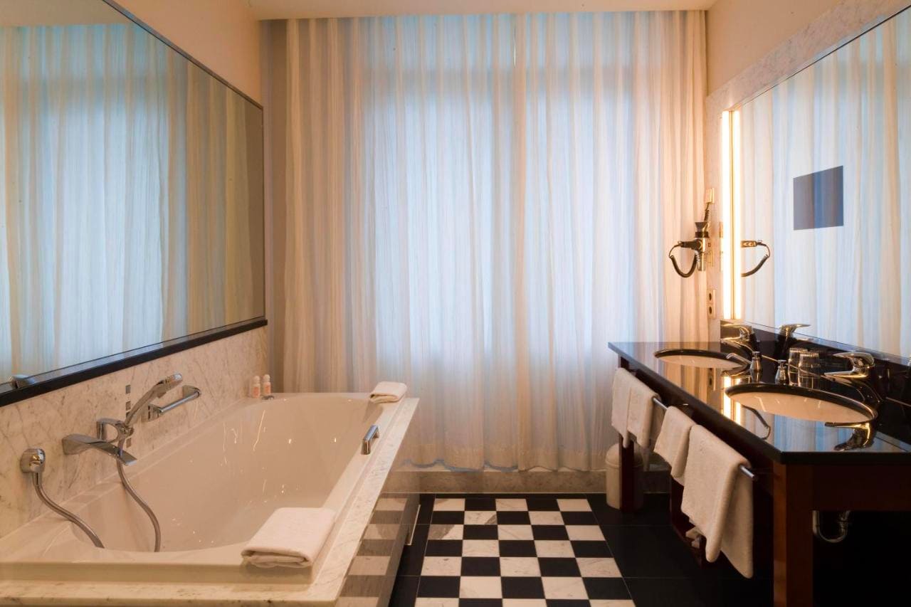 image-room-detail2 Elegantes Badezimmer mit großer Badewanne, Doppelwaschbecken und schwarz-weißem Fliesenboden.