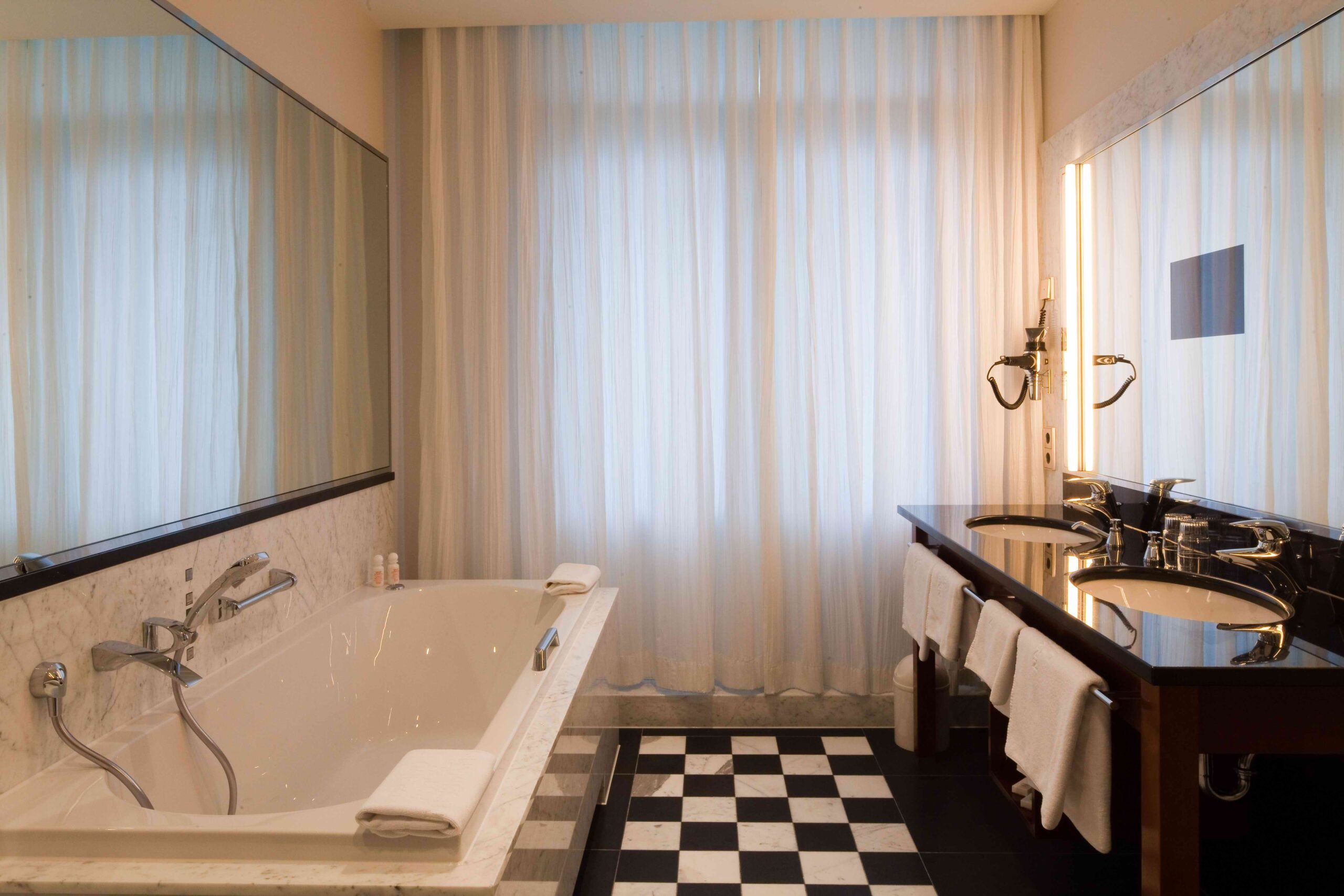 Elegantes Badezimmer mit großer Badewanne, Doppelwaschbecken und schwarz-weißem Fliesenboden.